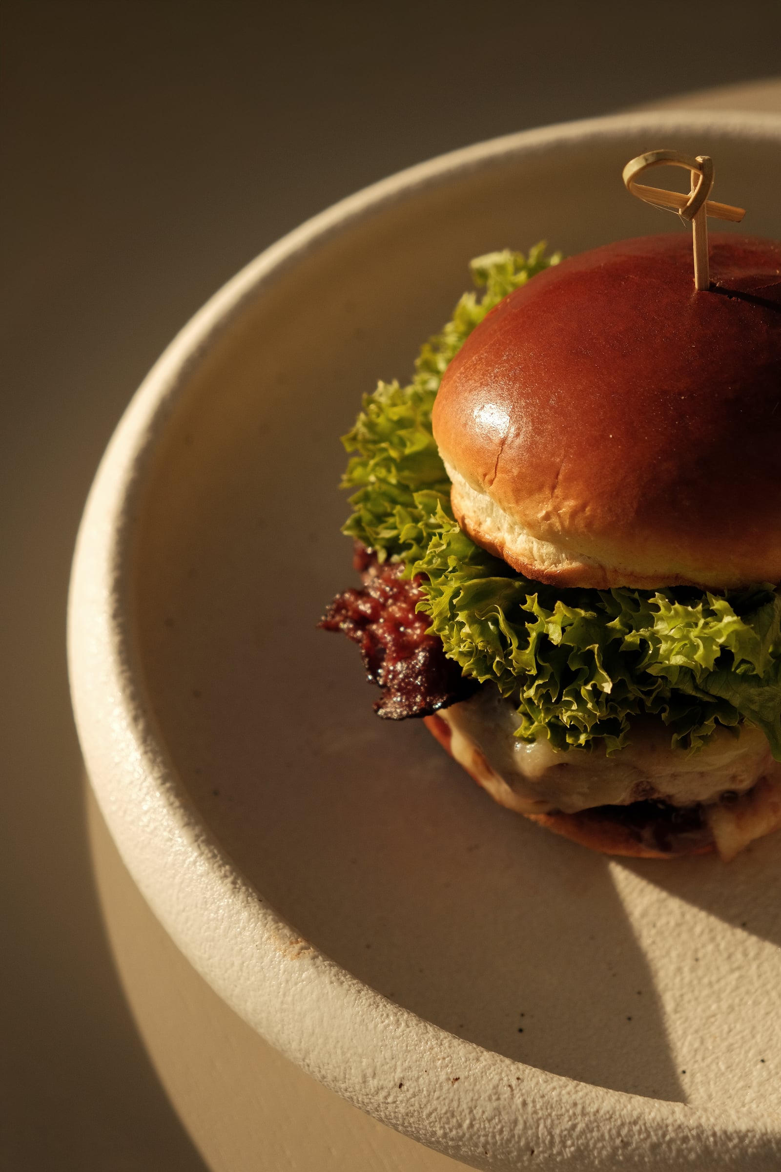 Burger gourmet sur bun brioché avec salade et bacon, assiette en céramique